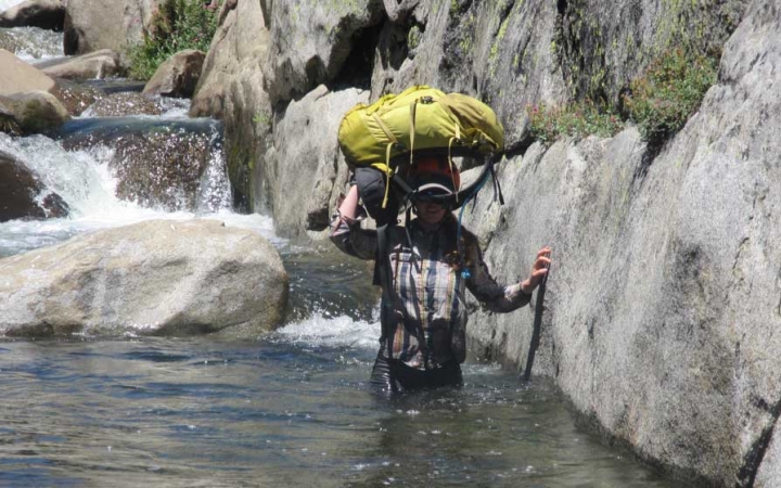 a person carries their backpack on their head as they wade through waist-deep water